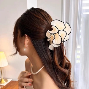 Detail of large cream hair claw clip with black piping on a messy bun hairstyle