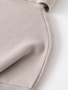 Macro shot of oat-colored ribbed knit texture and fine stitching detail on the garment hem