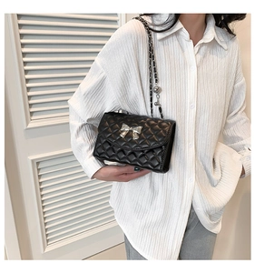 Detail of black quilted shoulder bag featuring silver metal bow and chain strap