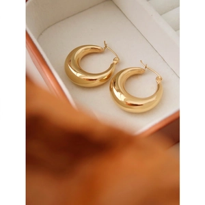 Macro detail of thick gold hollow circle earrings presented in a luxury white velvet gift box