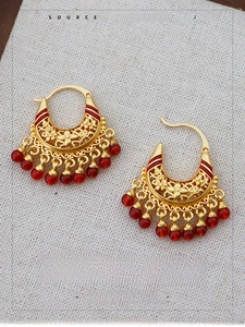 Detailed macro of gold hollow flower earrings with elegant red bead tassel pendants
