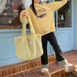 Detail of colorful plush tote bag with yellow and blue stripes held by model in casual wear