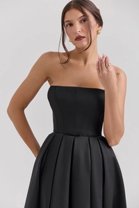 Detailed view of the bow decoration and pleated waist on a black satin midi dress