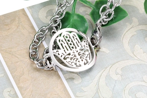 Macro shot of silver Hamsa hand charm and circular chain links on textured paper