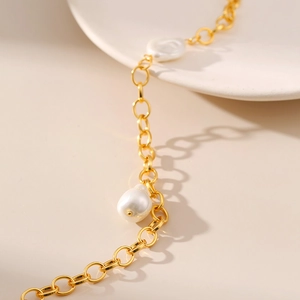 Close-up of baroque pearl pendant on 18K gold plated chain over a ceramic plate