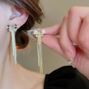 Detail of silver needle bow earrings with long golden tassels and sparkling crystals