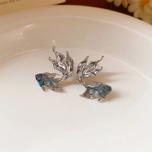 Vintage silver goldfish earrings with blue stones on a white ceramic tray, top view