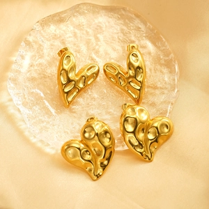 Golden heart-shaped stud earrings with irregular hammered texture on silk fabric