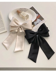 Detail of elegant satin bow hair clips in cream white and black with silky texture