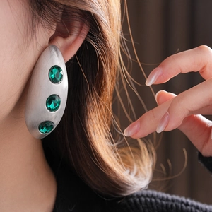 Macro detail of large matte silver oval earring with three inlaid green gems on model