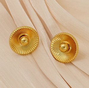 Macro shot of gold pleated round earrings with metallic sphere on beige silk fabric