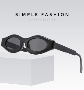 Detail view of stylish thick black oval frame sunglasses on a white geometric stand