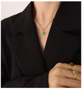 Detailopname van gouden kralenketting met turquoise hanger en stenen ringen op hand