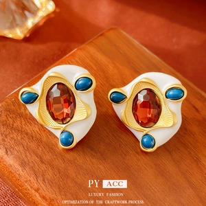Vintage gold oval earrings with white enamel, red gemstone and blue beads on a wood stand