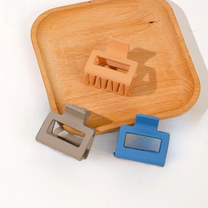 Matte square claw clips in light orange, taupe and blue on a wooden tray