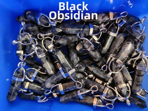 Close-up of hexagonal black larvikite crystal pendants with silver metal clasps in a tray