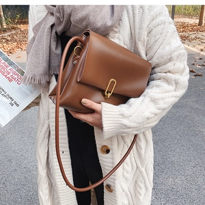 Détail du sac bandoulière en cuir marron avec boucle dorée dans un parc d'automne