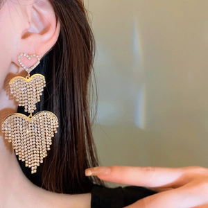 Macro detail of gold-toned heart tassel earrings with sparkling rhinestones on model