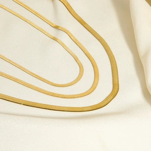Golden flat herringbone chain necklaces in three widths on elegant cream silk background