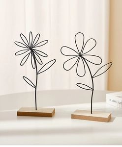 Close-up of minimalist black metal wire flower sculpture with light wood base