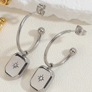 Close-up of silver stainless steel hoop earrings with starburst engraved rectangular charms