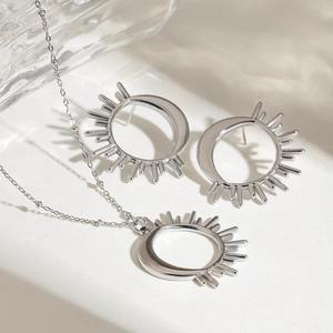 Close-up of silver celestial jewelry set featuring sun and moon pendants on white marble