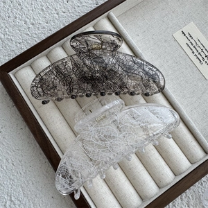 Macro detail of elegant lace-patterned resin hair claws in a beige jewelry display tray