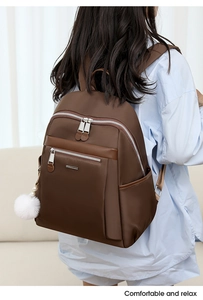 Detail of dark brown backpack with white pom-pom charm worn on model for casual travel