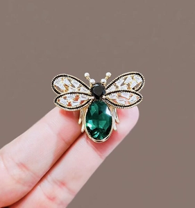 Detailed macro shot of vintage gold bee brooch with green gemstone and crystal wings