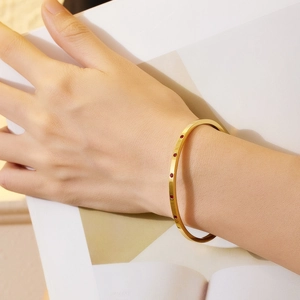 Detail of a gold plated C-shaped bangle featuring five red zircon stones on a wrist