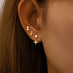 Detailed close-up of gold moon and star cartilage earrings with opal and zircon inlays