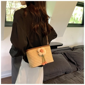 Detail of woven straw bucket bag featuring a 3D white floral accent and brown strap