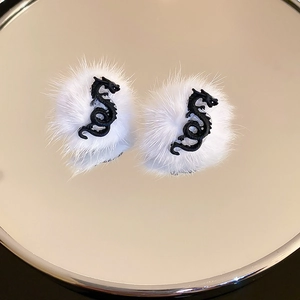 Detail of white plush earrings featuring a black dragon emblem on a mirrored surface