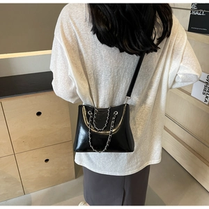 Detail of a black glossy patent leather shoulder bag with a silver chain strap on a model