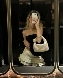 Detalle de un bolso beige de cuero trenzado con asa anudada y una minifalda corta de tablas