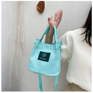 Detail view of mint green canvas bucket bag featuring a square patch and adjustable strap