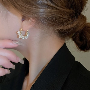 Detailed close-up of C-shaped flower earrings with pearls and crystals on a model