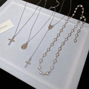 Detail view of Y2K silver cross necklace and pearl beaded chain on display tray