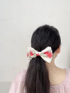 Detail of a white lace bow hair clip with red floral embroidery on a half-up hairstyle