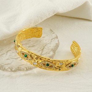 Detail of vintage textured gold cuff bracelet with green evil eye and crystal accents