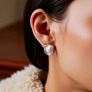 Baroque style gold-rimmed pearl earring with crystals shown on ear of model