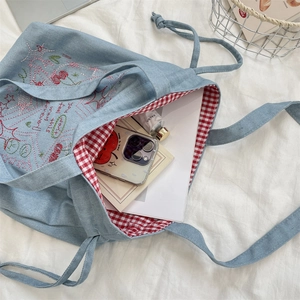 Detail of blue denim tote bag with red embroidery and red checkered lining interior