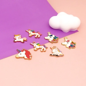 Detail view of seven gold alloy unicorn charms with colorful enamel on pink and purple background
