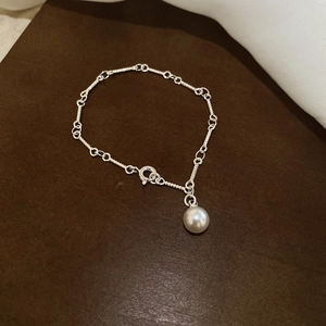 Detailed close-up of a silver-toned pearl charm bracelet on a textured leather surface