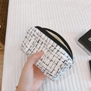 Handheld view of a tweed cosmetic bag showing textured weave and black zipper detail