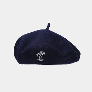 Detail of navy blue wool beret featuring white coconut tree embroidery on fabric