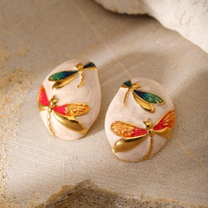 Macro detail of oval gold-plated dragonfly earrings with colorful enamel wing patterns