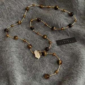 Tiger eye stone necklace with gold leaf pendant and zircons on soft plush backdrop