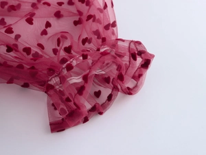 Détail du tissu en maille rouge avec motifs de cœurs en velours et bordure à volants
