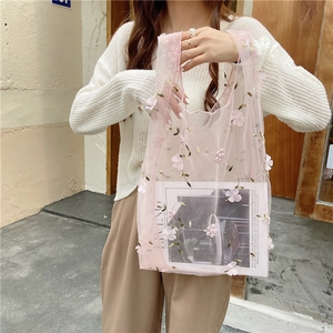 Detail of pink mesh tote bag with floral embroidery held by model against a beige wall